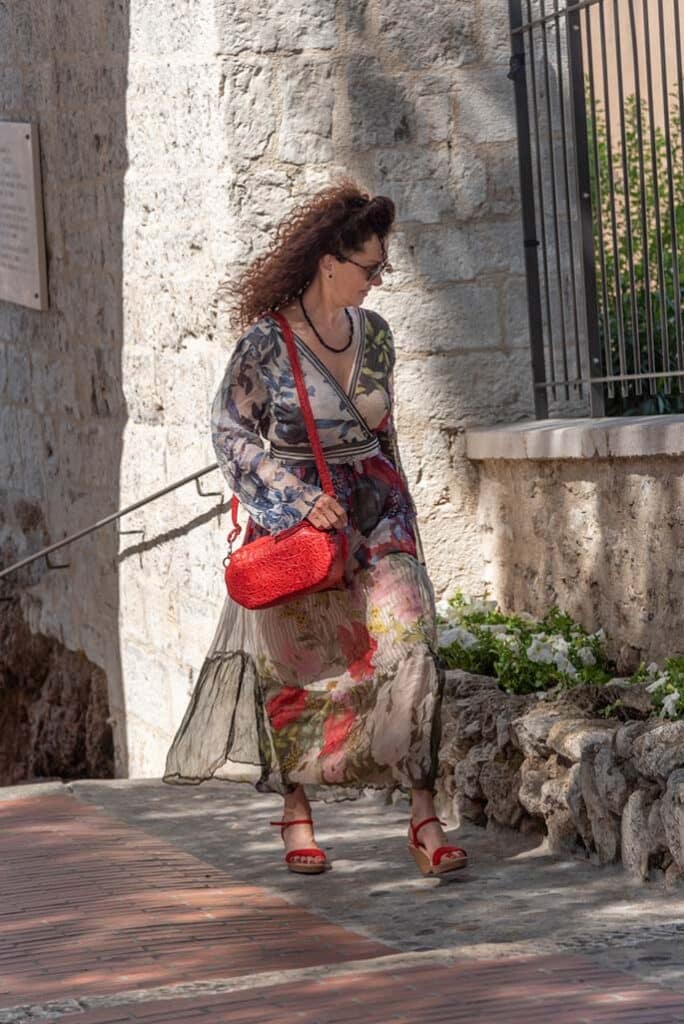 Femme marchant dyna,iquement dans les rues de Cannes avec son sac rouge coquelicot porté à l'épaule