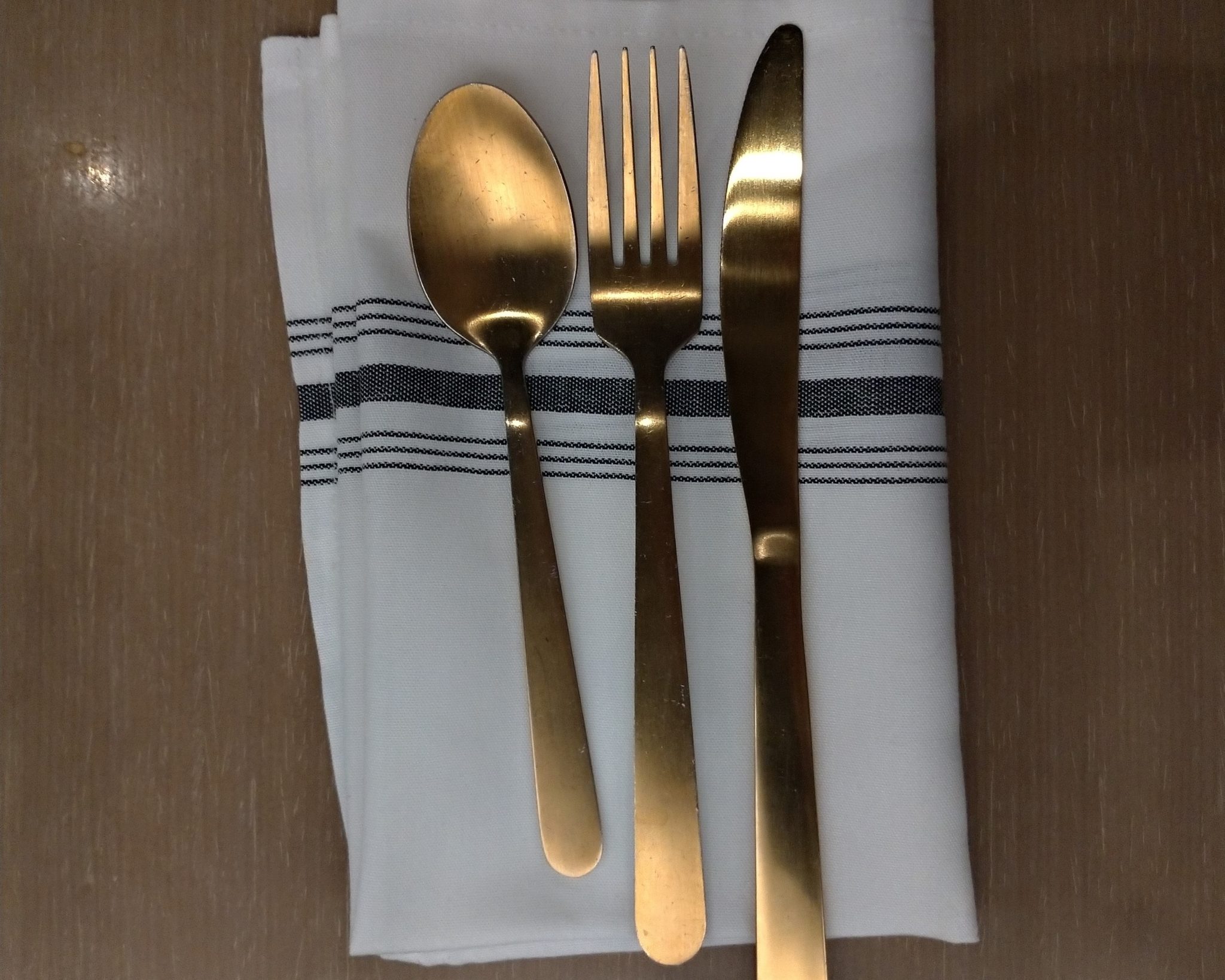 Fourchette, Couteau et cuillère couleur brinze posées sur une serviette de table blanche.