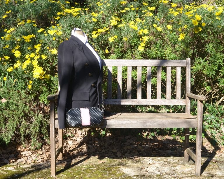 Mannequin posé sur un banc, avec une veste noire et les sac à pois argentés sur fond noir, porté en bandoulière.