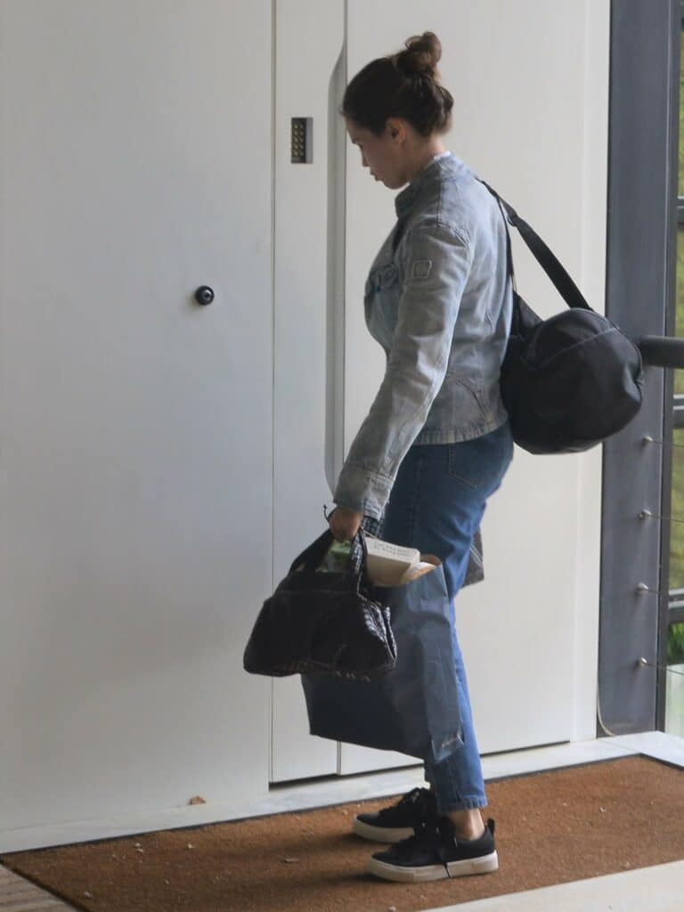 Femme qui vient de fermer sa porte d'entrée et qui part de chez elle surchargée de sacs