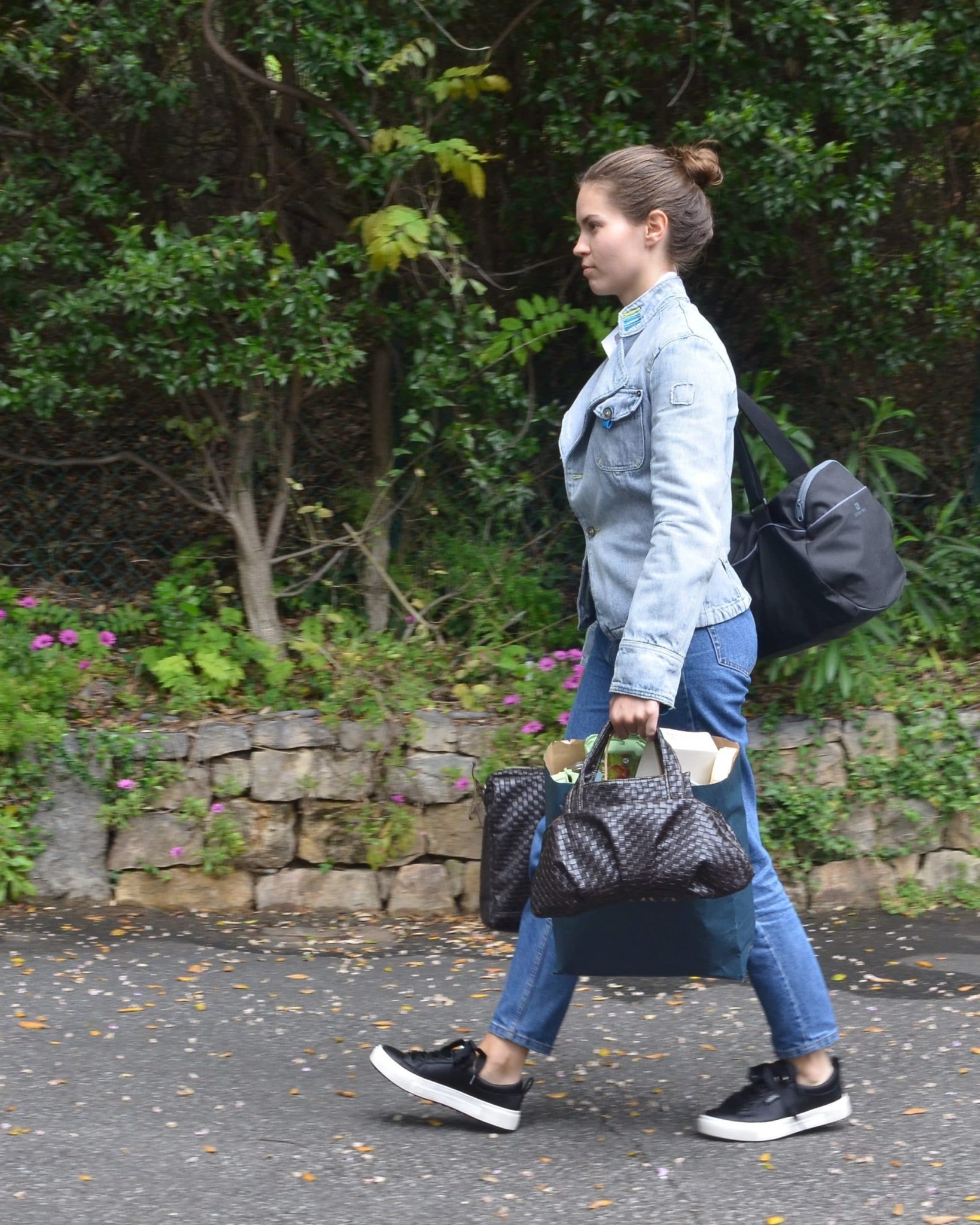 Femme portant son cartable, son sac de sport, un sac poubelle, son sac à main qui marche activement sur un chemin