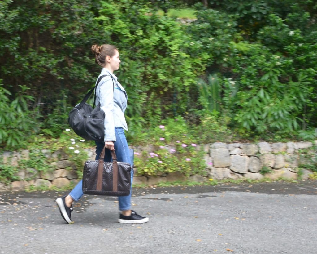 emme portant son cartable, son sac de sport, un sac poubelle, son sac à main qui marche activement sur un chemin