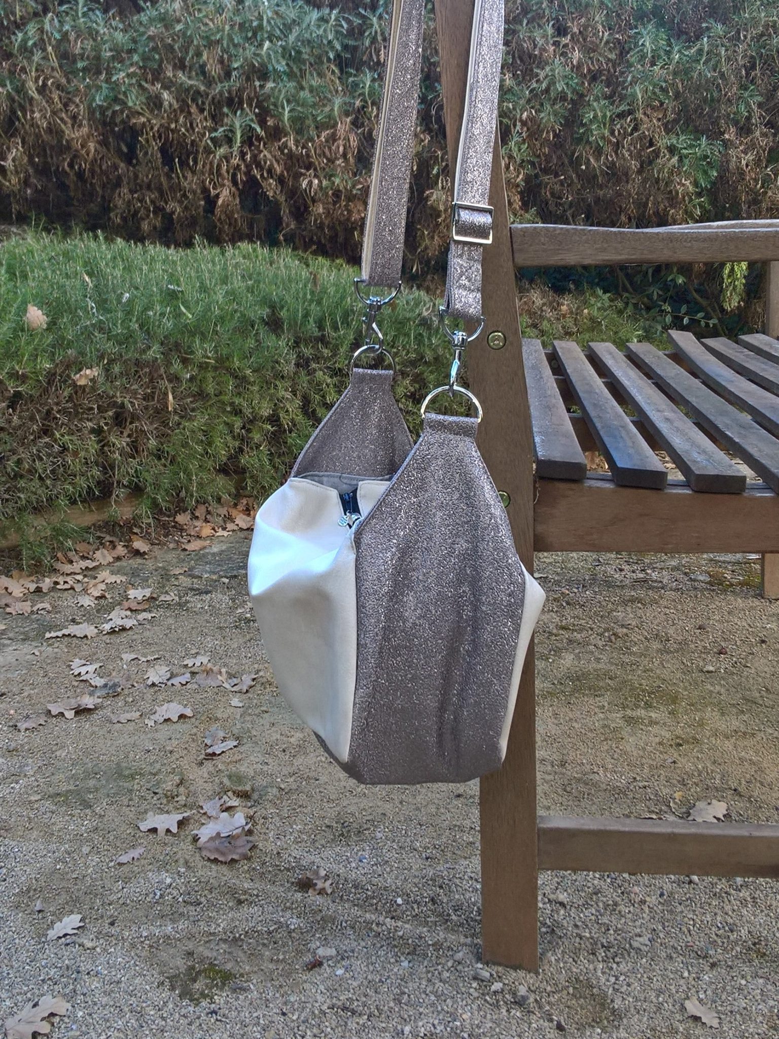 Sac bandoulière de forme cubique suspendu au dossier d'un banc de jardin, en bois