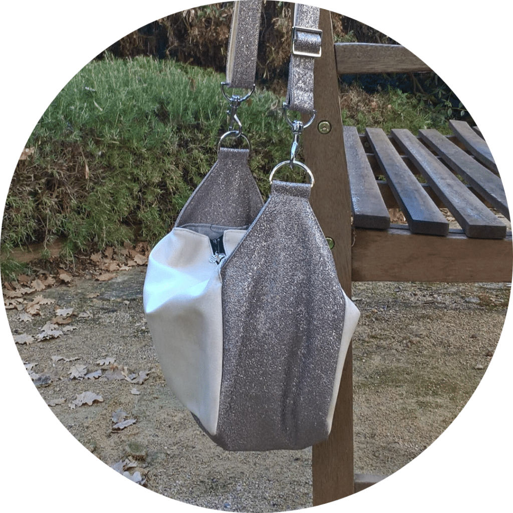 Sac bandoulière de forme cubique suspendu au dossier d'un banc de jardin.