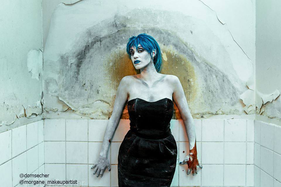 Bilal, Femme en robe de soirée noire décolletée aux épaules, debout dans une douche et une salle de bain délabrée, avec des cheveux bleus et une plaies sur la main droite, Body painting de l'artiste Morgane MakeUp artiste