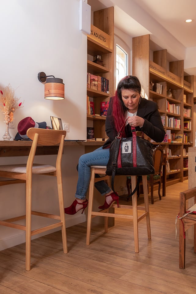 Femme assise sur un tabpuret haut, cerhchat quelque chose dans son cartable. Lirérie-cafè, Un moment chez mémé.